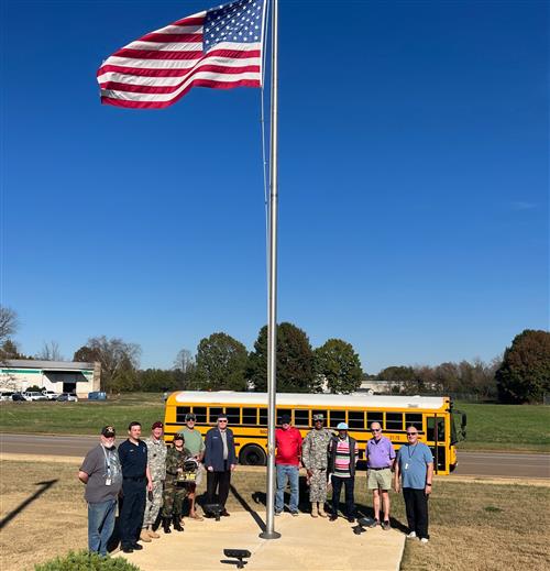 veterans who are bus drivers encircled around a flagpole with schoolbus in background